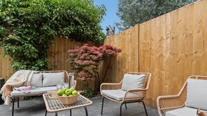 Una zona patio con mobili in vimini, un tavolo con una ciotola di frutta e un recinto in legno.