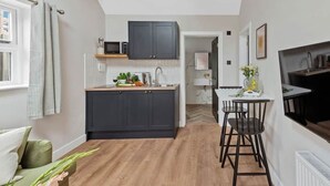 Una cucina compatta con mobili scuri, un forno a microonde e un piccolo spazio pranzo con tavolo e sedie.