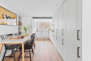 A modern kitchen with white cabinetry, a dining table with chairs, and a view to the living area. - Rose & Rampart Exclusive Use - sleeps up to 12 (Kenilworth)