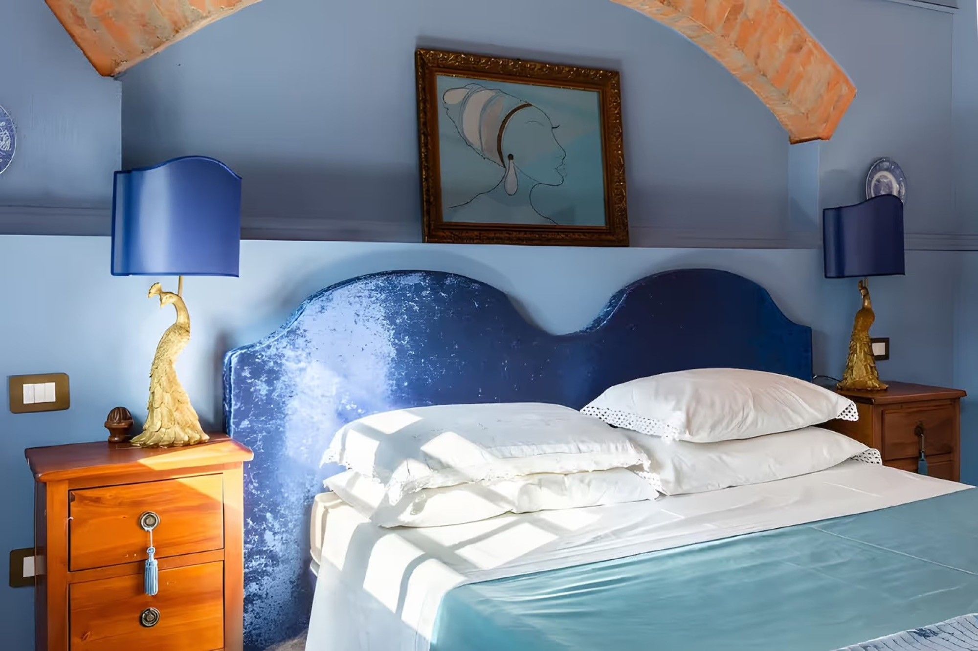 Une chambre à coucher avec un lit, deux tables de chevet, une commode, un tableau et un plafond en arc de cercle.