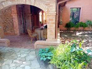Eine Terrasse im Freien mit einem Ziegelbogen, einem runden Tisch und Korbstühlen.