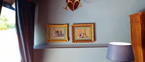 Una habitación con techo de madera, una decoración de cornamenta de ciervo, dos cuadros enmarcados, una lámpara azul y una silla de madera.