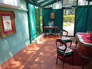 Ein Wintergarten mit Fliesenboden, einem Tisch mit Stühlen, einer Uhr und einem gerahmten Bild an der Wand.