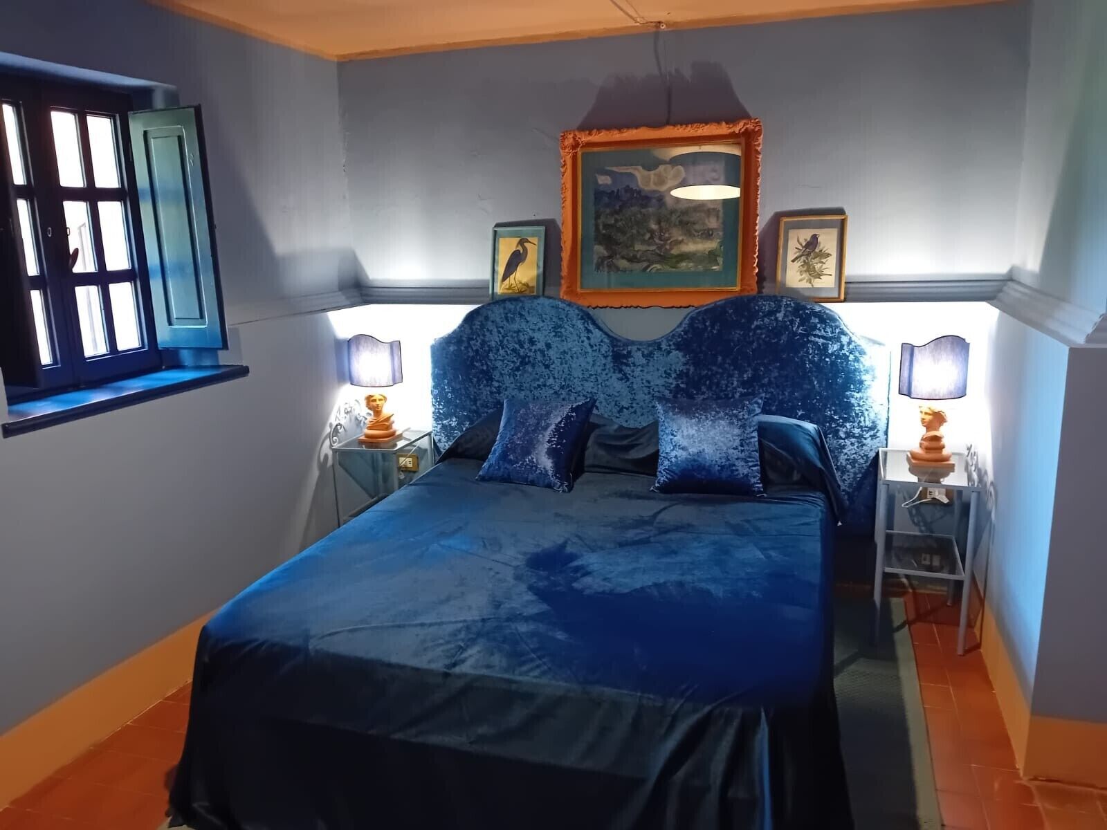 Une chambre à coucher avec un lit, deux tables de chevet, une fenêtre et des œuvres d’art murales.