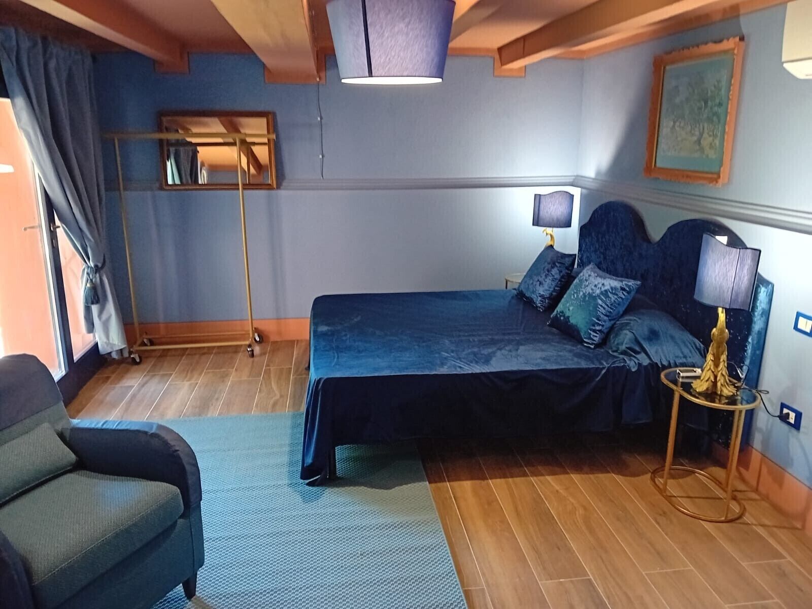 Un dormitorio con cama, lámparas de noche, una silla, una lámpara de pie y un cuadro en la pared.