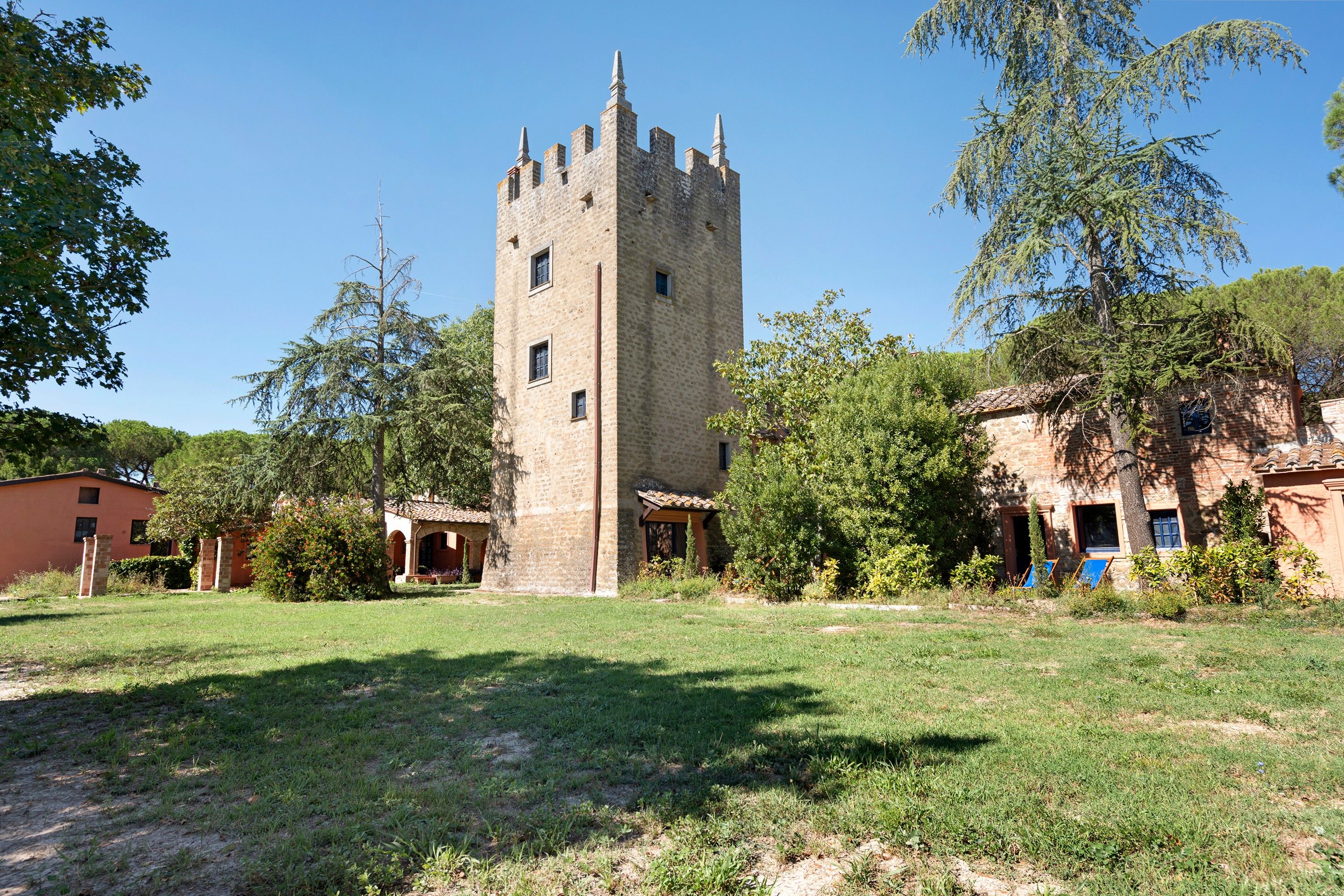Um castelo com uma torre central, rodeado por árvores e um espaço gramado.