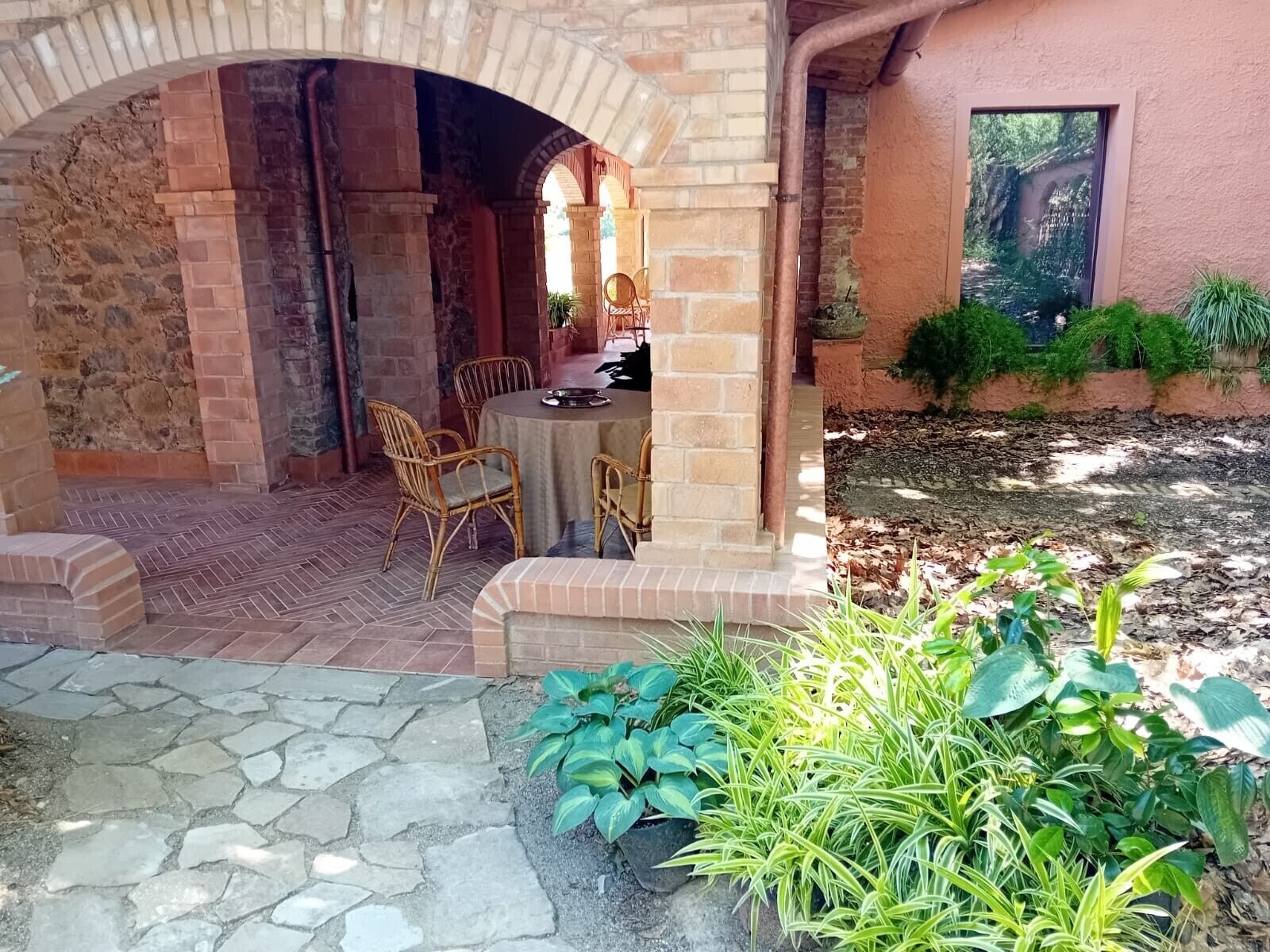 Une terrasse extérieure agrémentée d’une arche en briques, d’une table ronde et de chaises en osier.