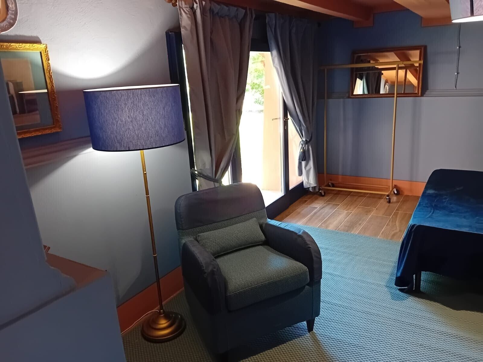 Una habitación con una silla, una lámpara de pie, una cama, un espejo y una ventana con cortinas.