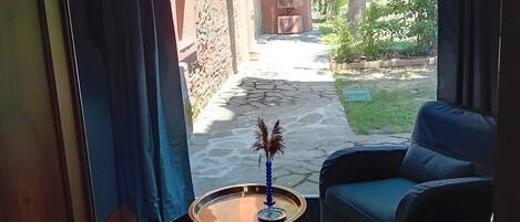 Une pièce avec un canapé bleu, une table basse ronde ornée d’un vase, et une vue sur un espace extérieur comprenant un chemin en pierre et de la verdure.