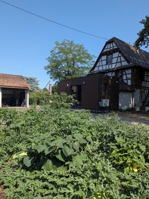 Ein traditionelles Fachwerkhäuschen mit einem modernen Anbau, umgeben von einem Gemüsegarten.