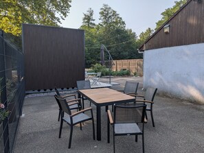 Eine Terrasse im Freien mit Tisch und Stühlen, umgeben von einem Zaun und einem Gebäude.