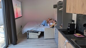 A compact bedroom with a bed, a small sofa, a kitchenette, and a window with curtains. - Detached studio apartment with a garden, air conditioning, and a garage (Gries)