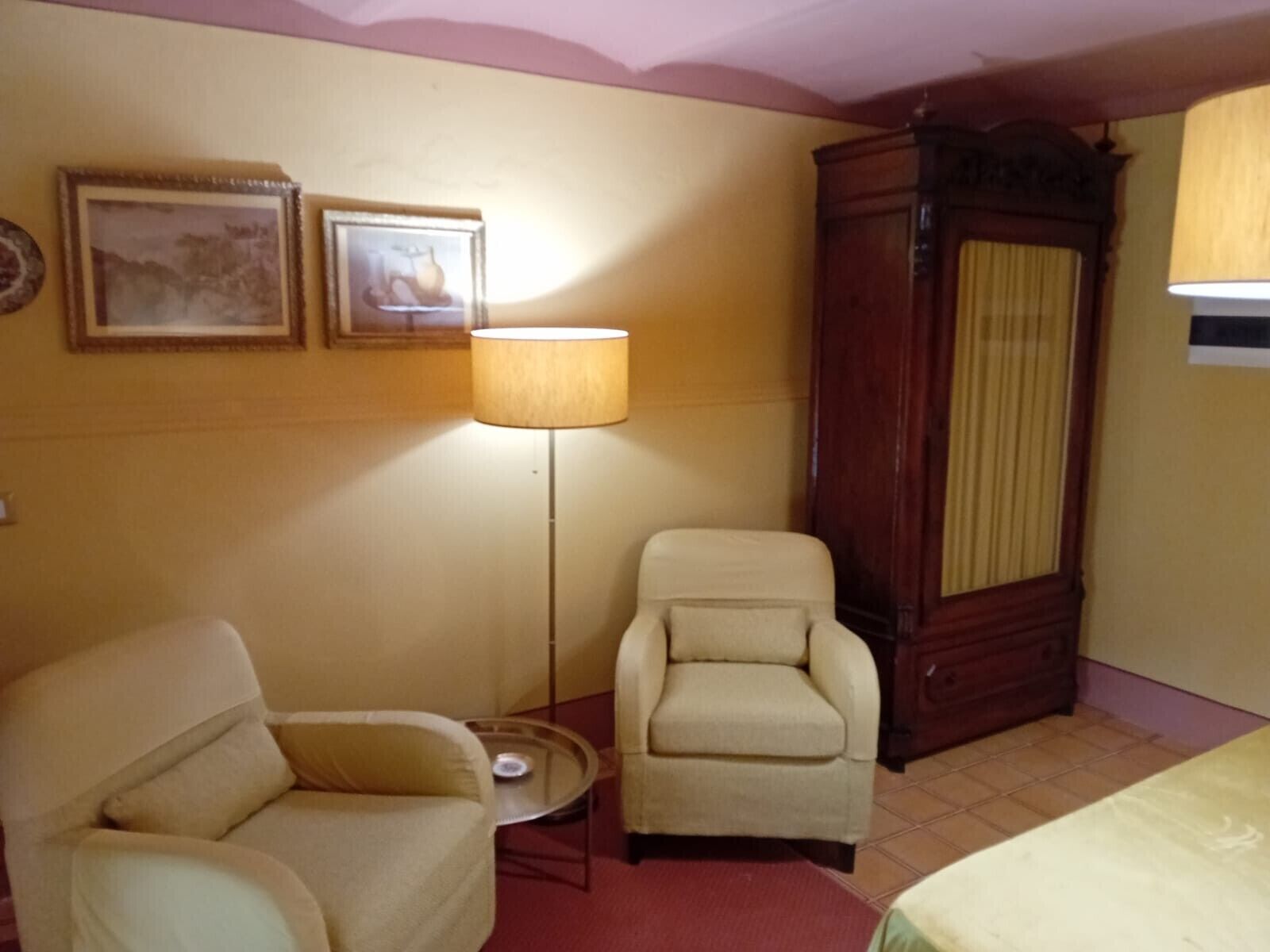 Une pièce comprenant deux fauteuils, une lampe sur pied, une armoire en bois et deux tableaux encadrés accrochés au mur.