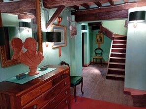 Una habitación con un aparador de madera, un busto, un cuadro enmarcado, una silla y una escalera.