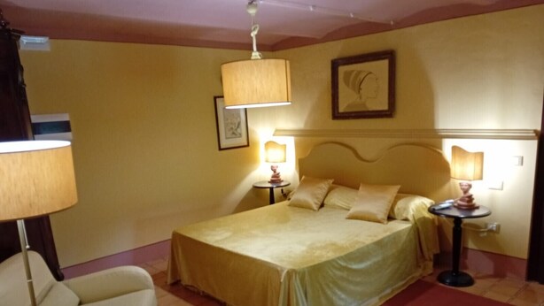 Una habitación de hotel con una cama, dos mesitas de noche con lámparas, una silla y una pequeña mesa redonda.