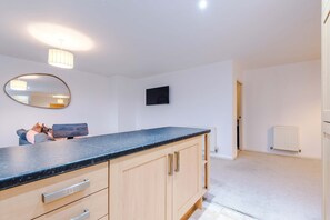 A modern kitchen with a granite countertop, wooden cabinets, a built-in oven, and a wall-mounted TV. - Luxury 2BR Altrincham 15m to MAN Near Market (Altrincham)
