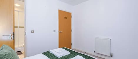 A hotel room with a bed, a wooden door, a radiator, and a bathroom visible through an open door.