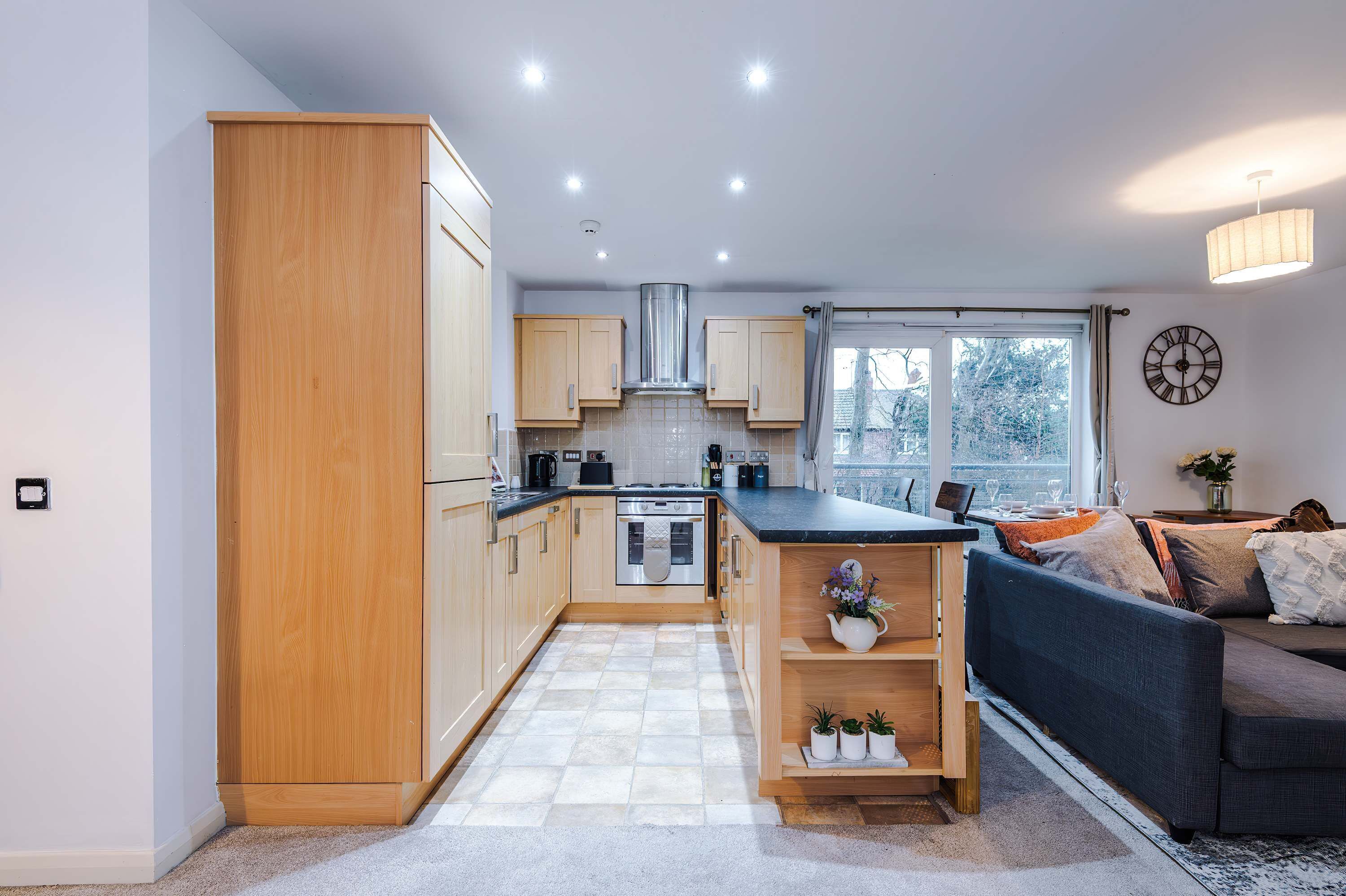 A modern kitchen with wooden cabinets, a central island, and a dining area with a sofa and table.