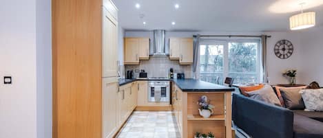 A modern kitchen with wooden cabinets, a central island, and a dining area with a sofa and table.