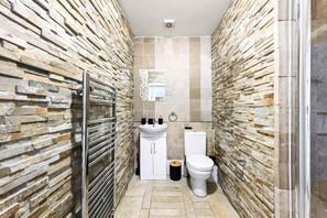 Ein schmales Badezimmer mit Steinwänden, einem weißen Waschbecken, einer Toilette und einer Duschkabine.