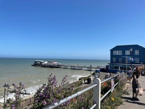 A coastal view with a pier extending into the sea, a blue building with signage, and a walkway with railings. - Luxury 6BR Beach House Hot Tub Sea View (Cromer)