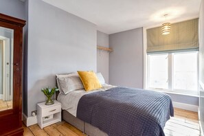 A bedroom with a bed, a nightstand, a window with a view, and a wooden floor. - Luxury 6BR Beach House Hot Tub Sea View (Cromer)