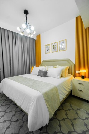 Ein Hotelzimmer mit einem Bett, einem Nachttisch, einer Lampe, einer Deckenleuchte und drei gerahmten Bildern an der Wand.