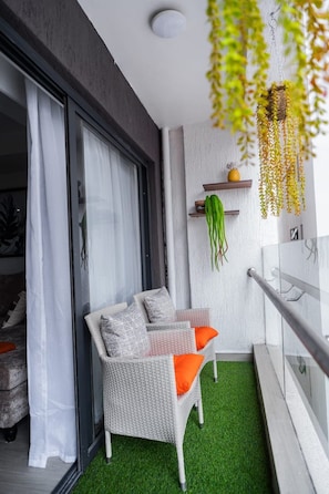 A balcony with a wicker chair, a small shelf with plants, and a railing. - New Luxury Furnish 1BR @Kilimani w/ Pool, Sauna & Gym | Walk to Yaya & Dining (Nairobi)