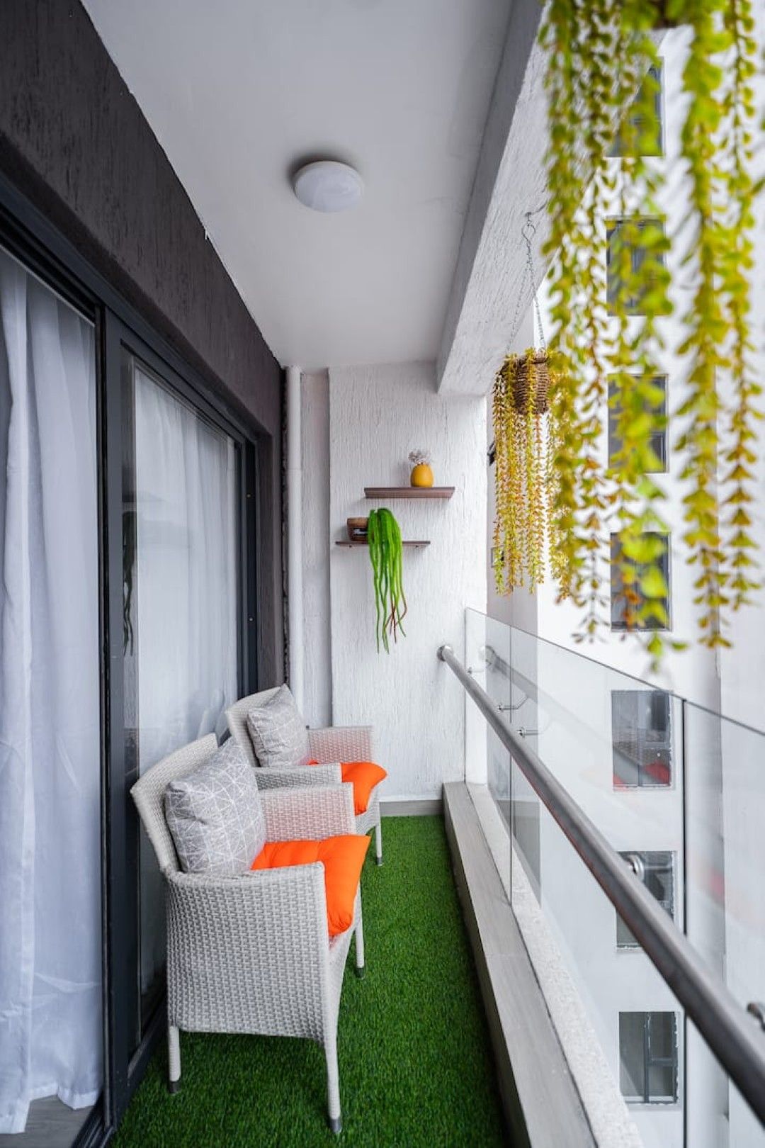 Un balcón con un sofá de mimbre blanco, césped artificial verde y plantas colgantes.