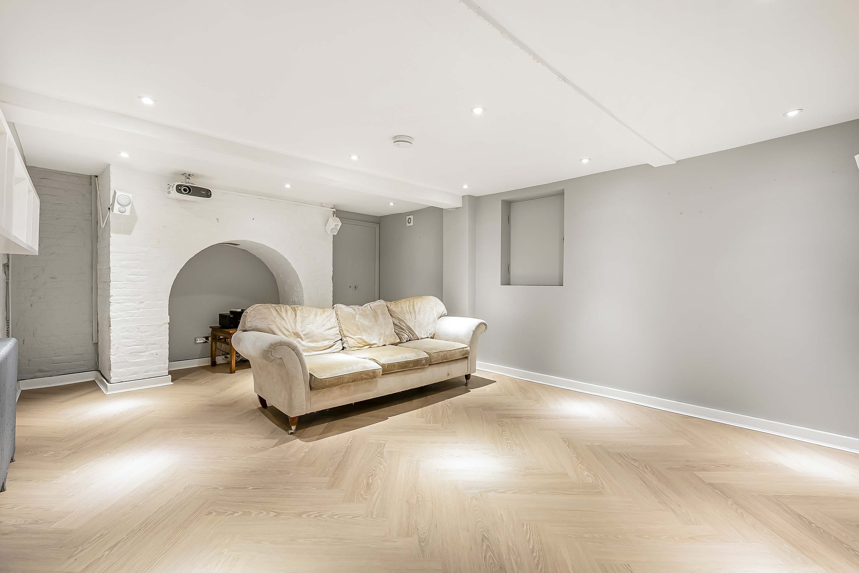 Un salón espacioso con un sofá de color claro, suelo de madera y techo blanco con iluminación empotrada.