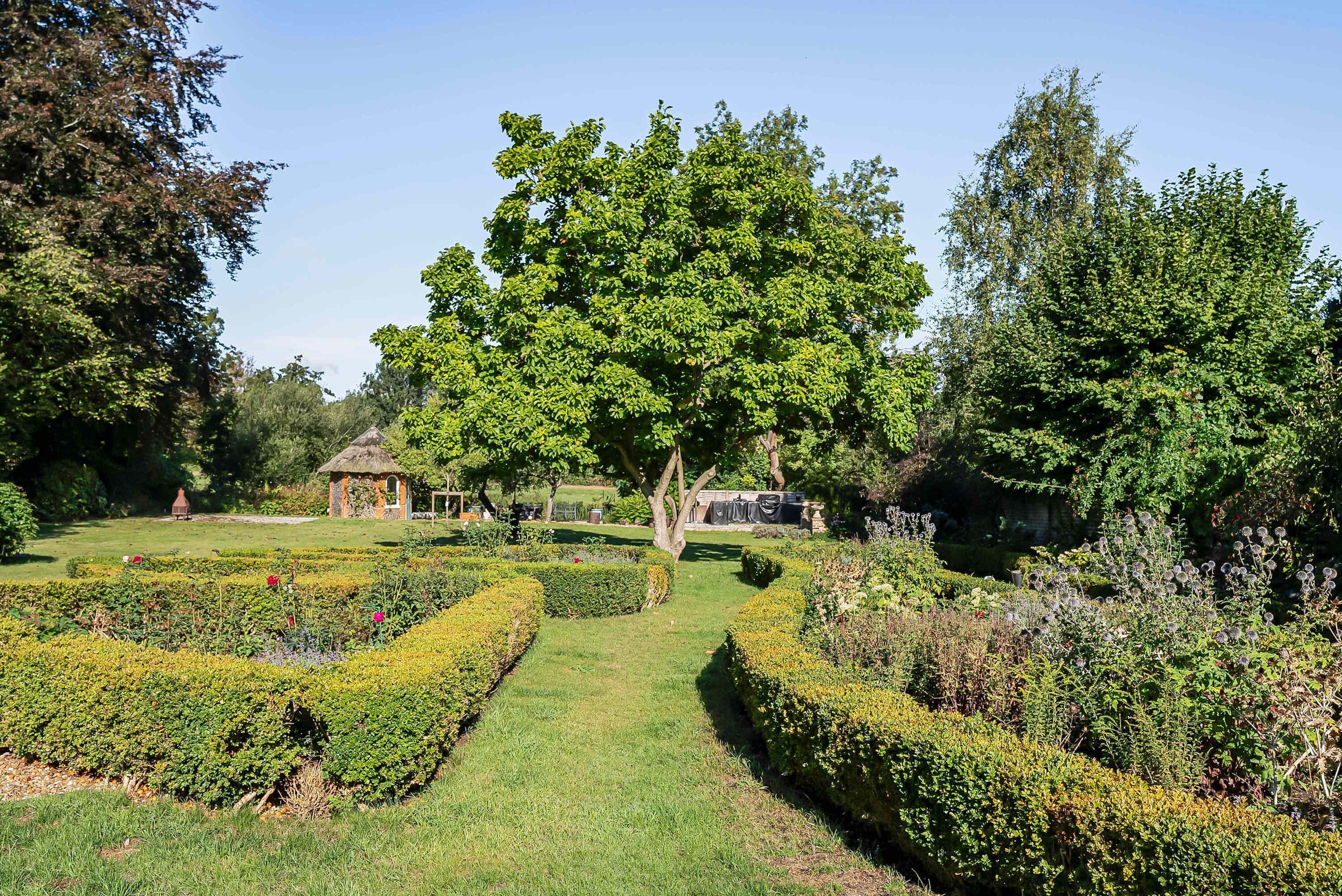 Un jardin bien entretenu, avec un chemin central, des haies soigneusement taillées et une grande variété de plantes.