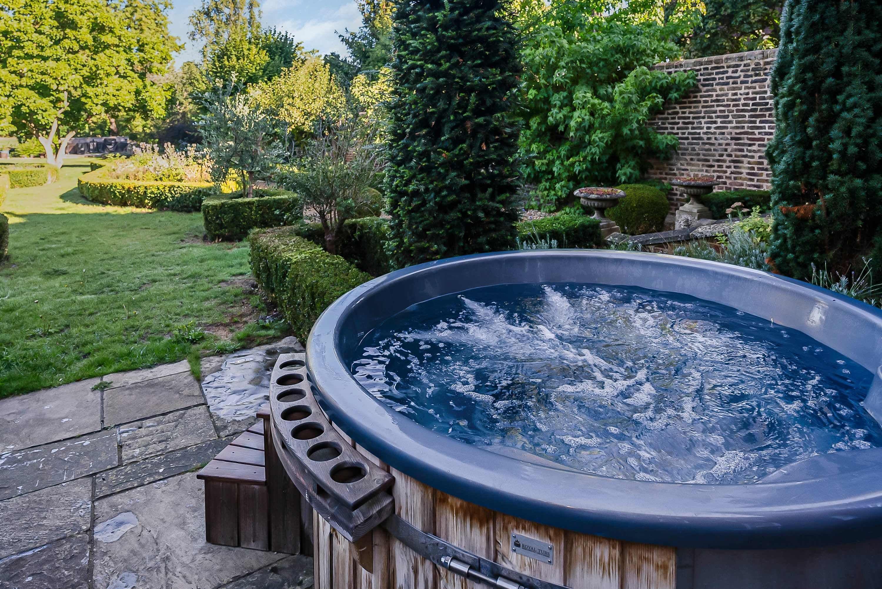 A hot tub in a garden with a brick wall and various plants.