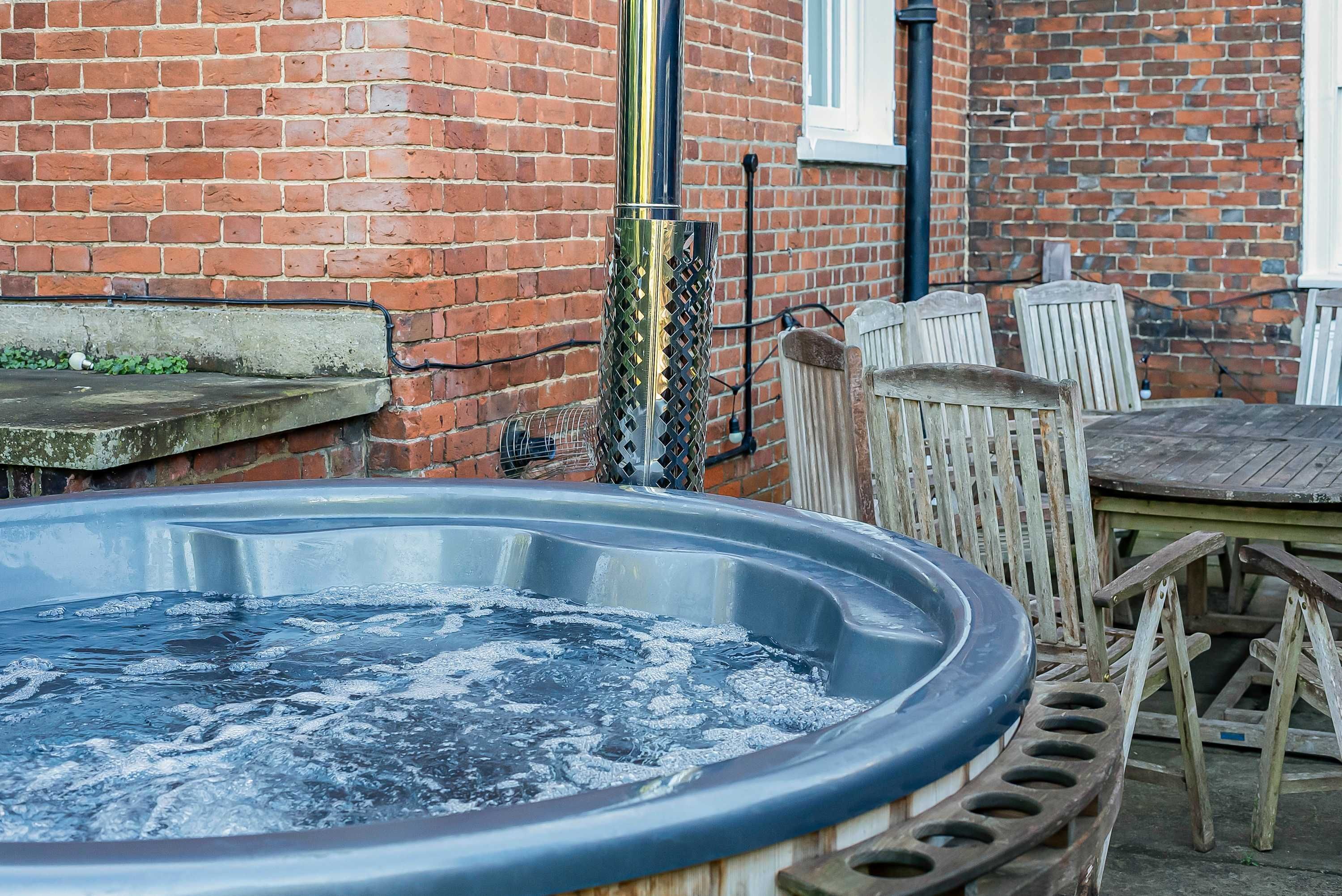 Un jacuzzi en un patio trasero con un muro de ladrillo, sillas de madera y una mesa.