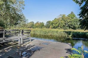 A wooden dock extending into a calm river with lush greenery and trees in the background.