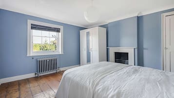 Un dormitorio con una cama grande, una ventana con persianas, un radiador, un armario y una chimenea.