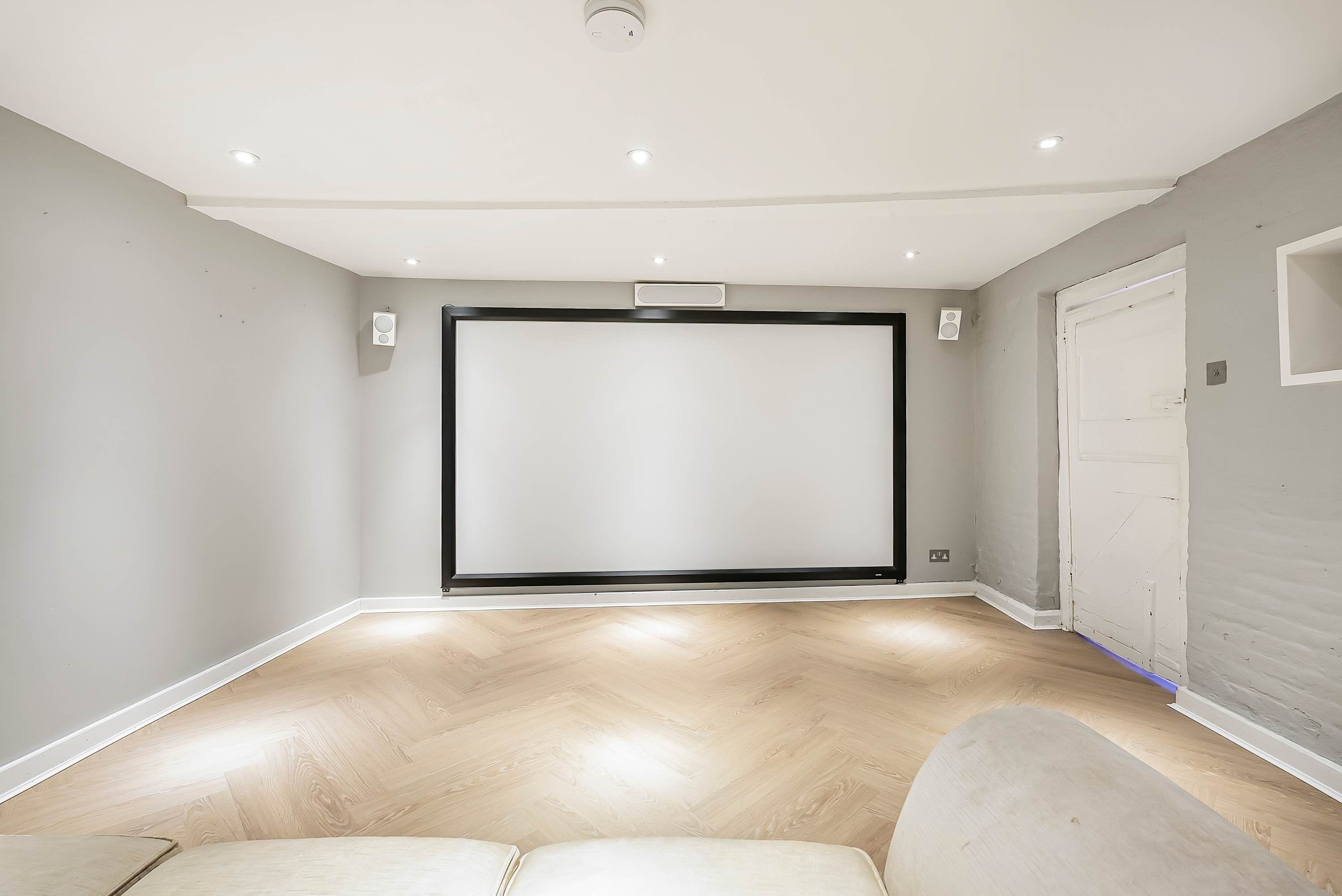 Una habitación con un televisor de pantalla plana grande montado en la pared, suelo de madera y una puerta a la derecha.
