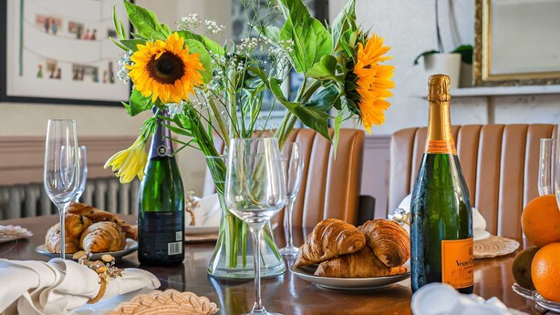 Un tavolo imbandito con diverse cose: bottiglie di vino, bicchieri, fiori e pasticcini.