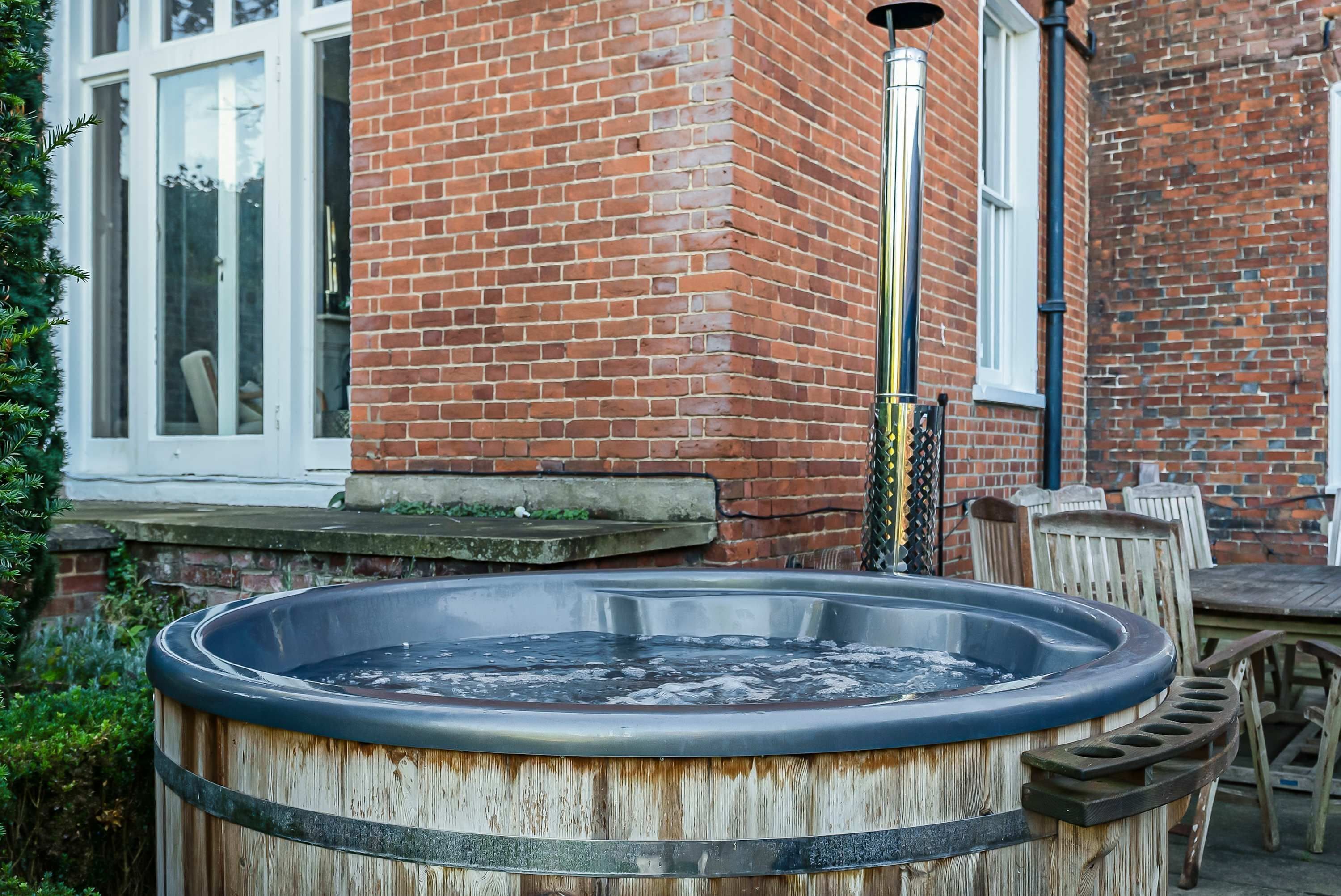 Un jacuzzi de madera en un patio trasero, con una casa de ladrillo al fondo.