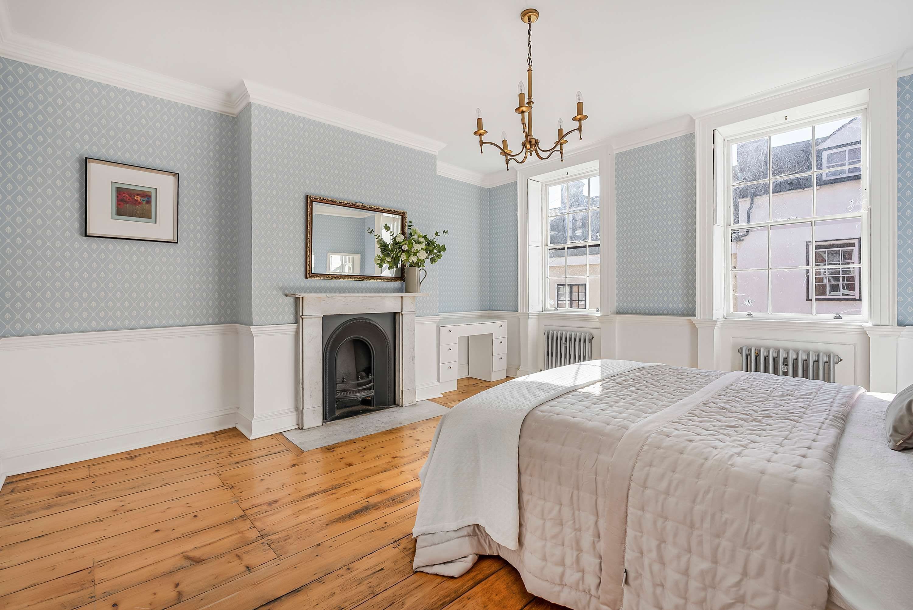 Une chambre avec une cheminée, un lit, une fenêtre donnant sur un beau paysage et un lustre.