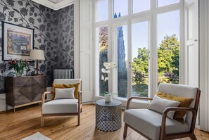 A room with two armchairs, a sideboard, a framed picture, and a window with a view of trees. - Luxury 7 Bed Herts Stay Cinema Hot Tub (Hertford)
