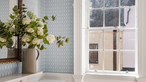 Un bagno con un mobile vanitario bianco, un vaso con fiori bianchi, uno specchio con cornice decorativa e una finestra vista esterna.