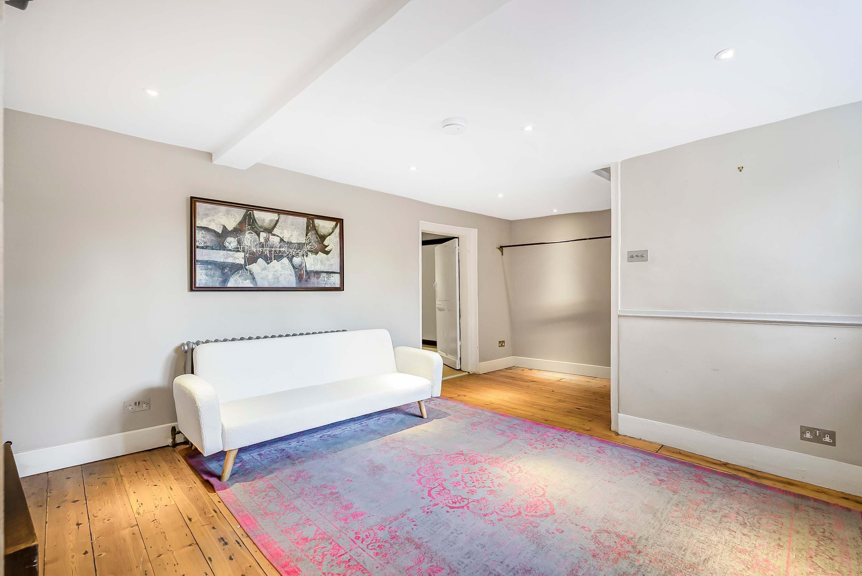 A modern living room with a white sofa, a colorful rug, and a painting on the wall.
