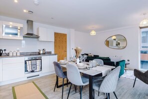A modern kitchen with built-in appliances, a dining area with a table set for four, and a large mirror on the wall. - Breathtaking Skyline Views Wi-fi Great Value (Salford)