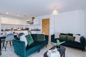 A modern living room with a green sofa set, a dining area with a table and chairs, and a kitchen in the background. - Breathtaking Skyline Views Wi-fi Great Value (Salford)