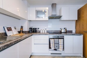 Una cuina moderna amb armaris blancs, forn integrat, cafetera i tetera.