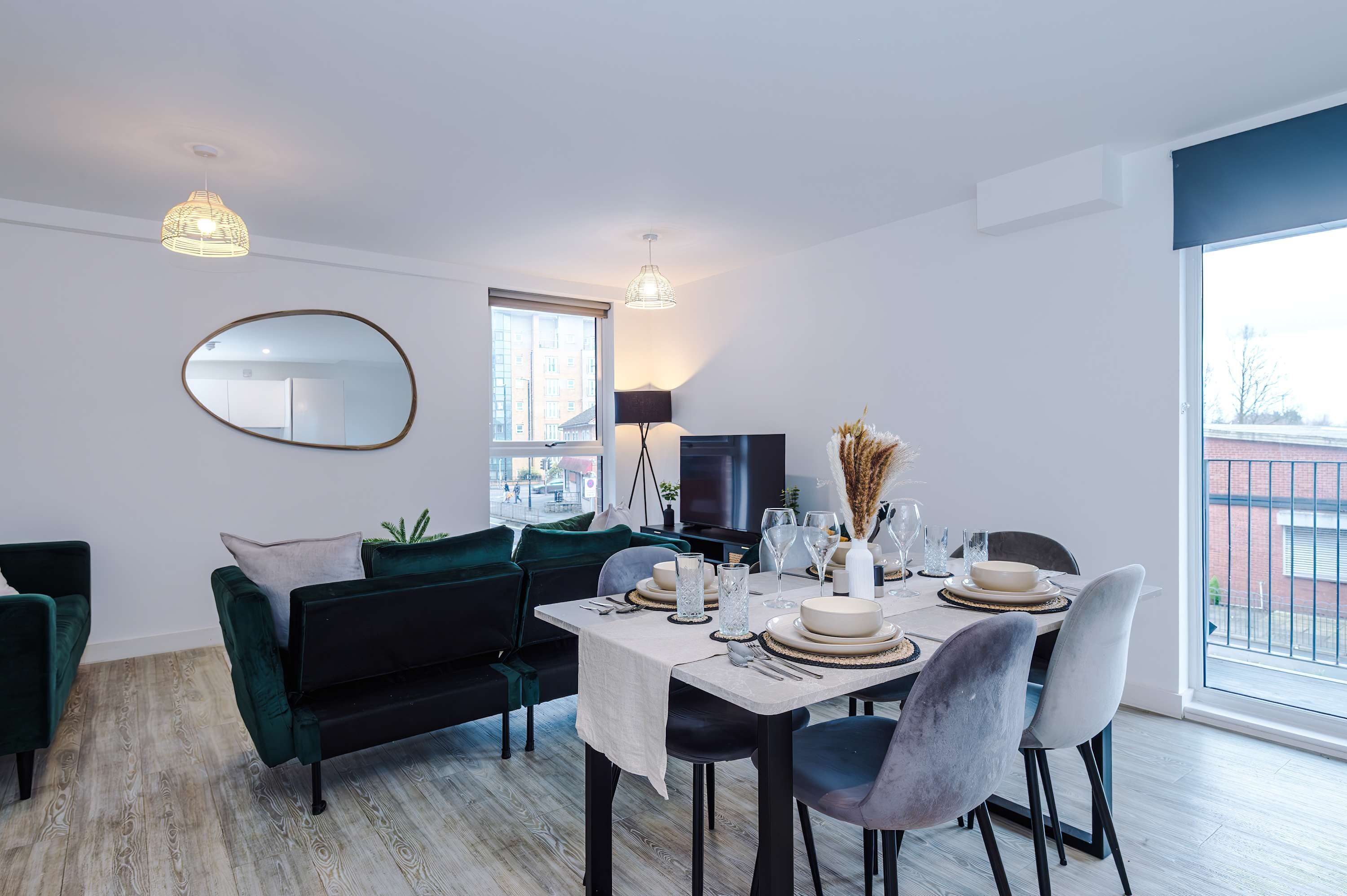A modern dining area with a table set for four, a sofa, a television, and a large window with a view.