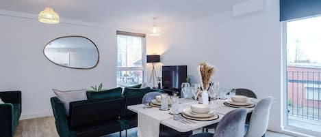 A modern dining area with a table set for four, a sofa, a television, and a large window with a view.
