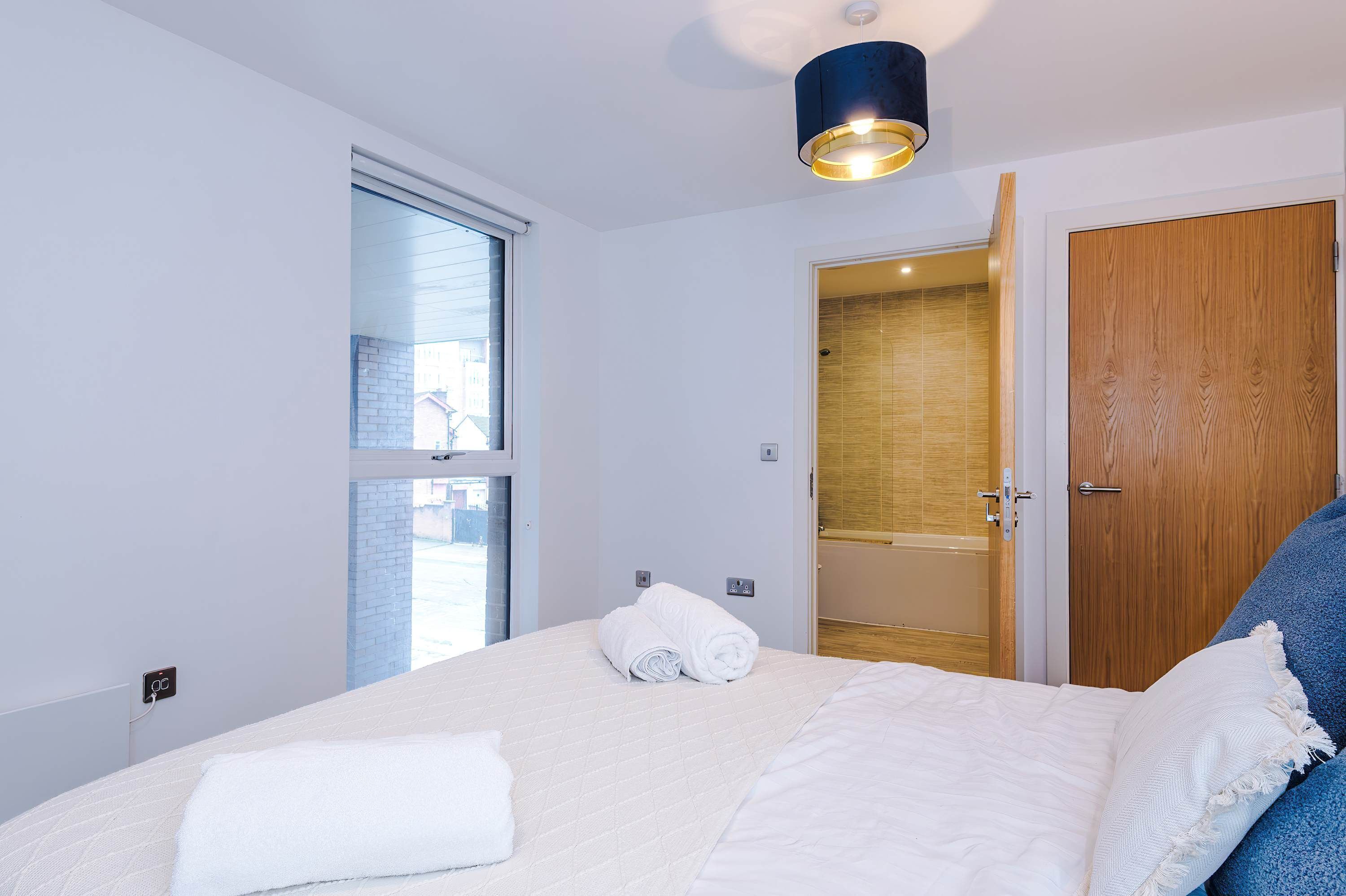A hotel room with a bed, a window, a door, and a ceiling light fixture.