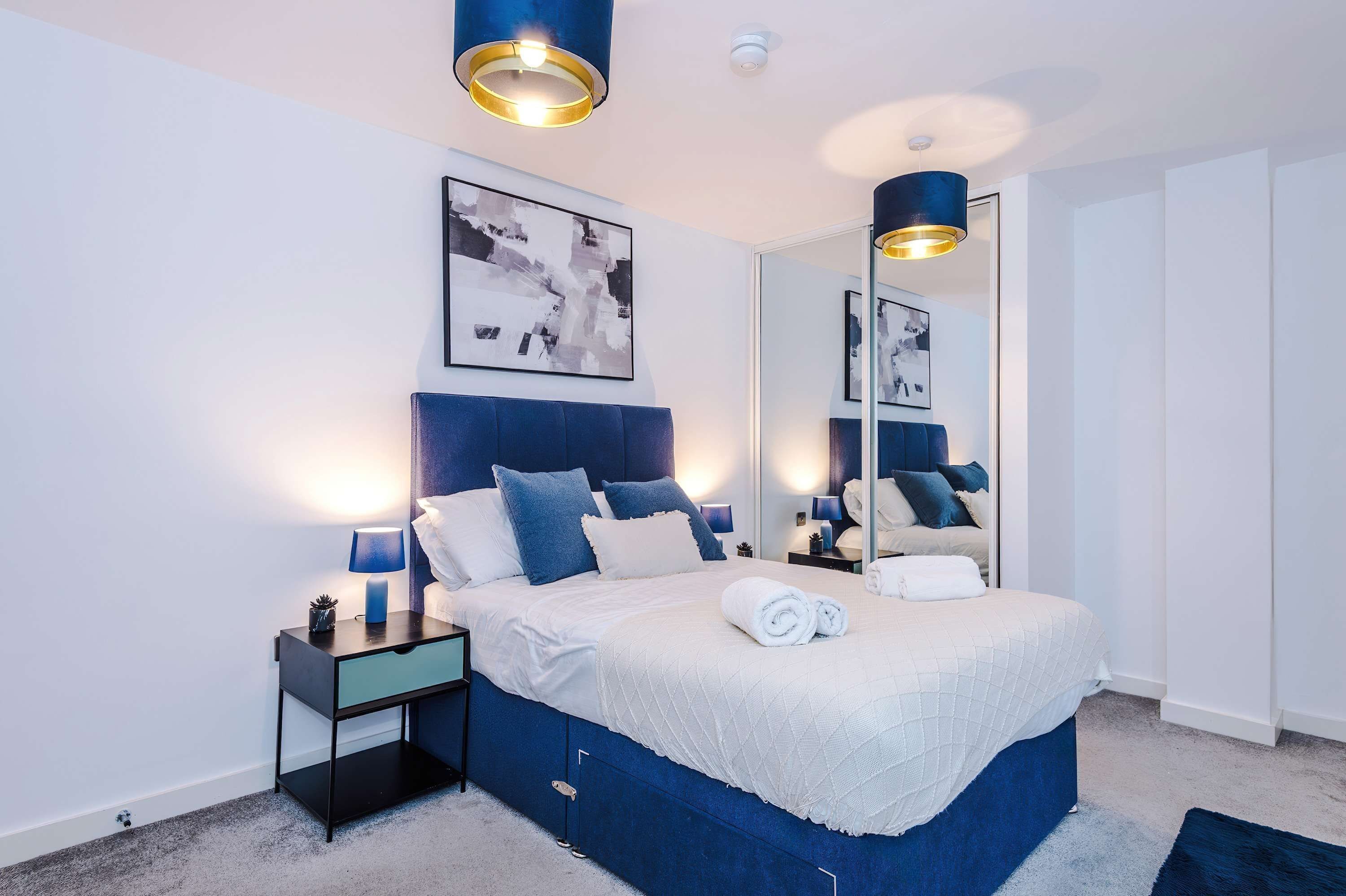 Une chambre à coucher moderne avec un grand lit, des lampes de chevet, une table de chevet, un miroir et des œuvres d’art abstraites accrochées au mur.