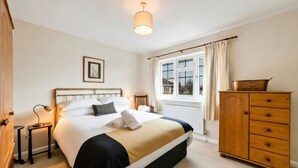 Ein Schlafzimmer mit einem Bett, einer Holzkommode, einem Nachttisch, einer Lampe und einem Fenster mit Vorhängen.